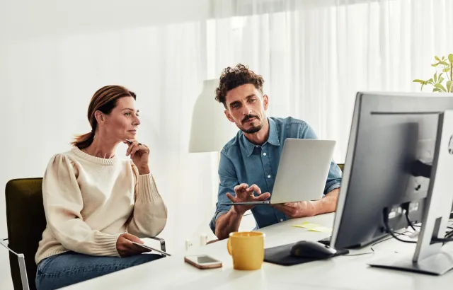 Person showing woman how to use feature on their laptop, at a desk